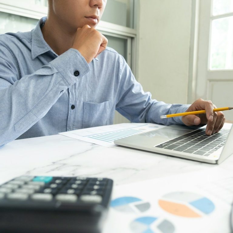 Wärmepumpenplanung bei der Wärmetechnik Bell Mann denkt nach, während er an einem Laptop arbeitet, umgeben von Notizen und einem Taschenrechner.